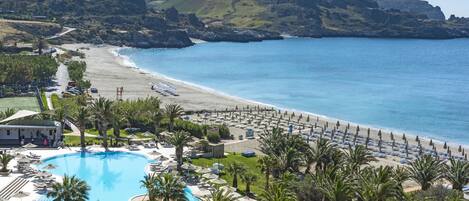 A resort with a swimming pool, beach, and mountainous backdrop.