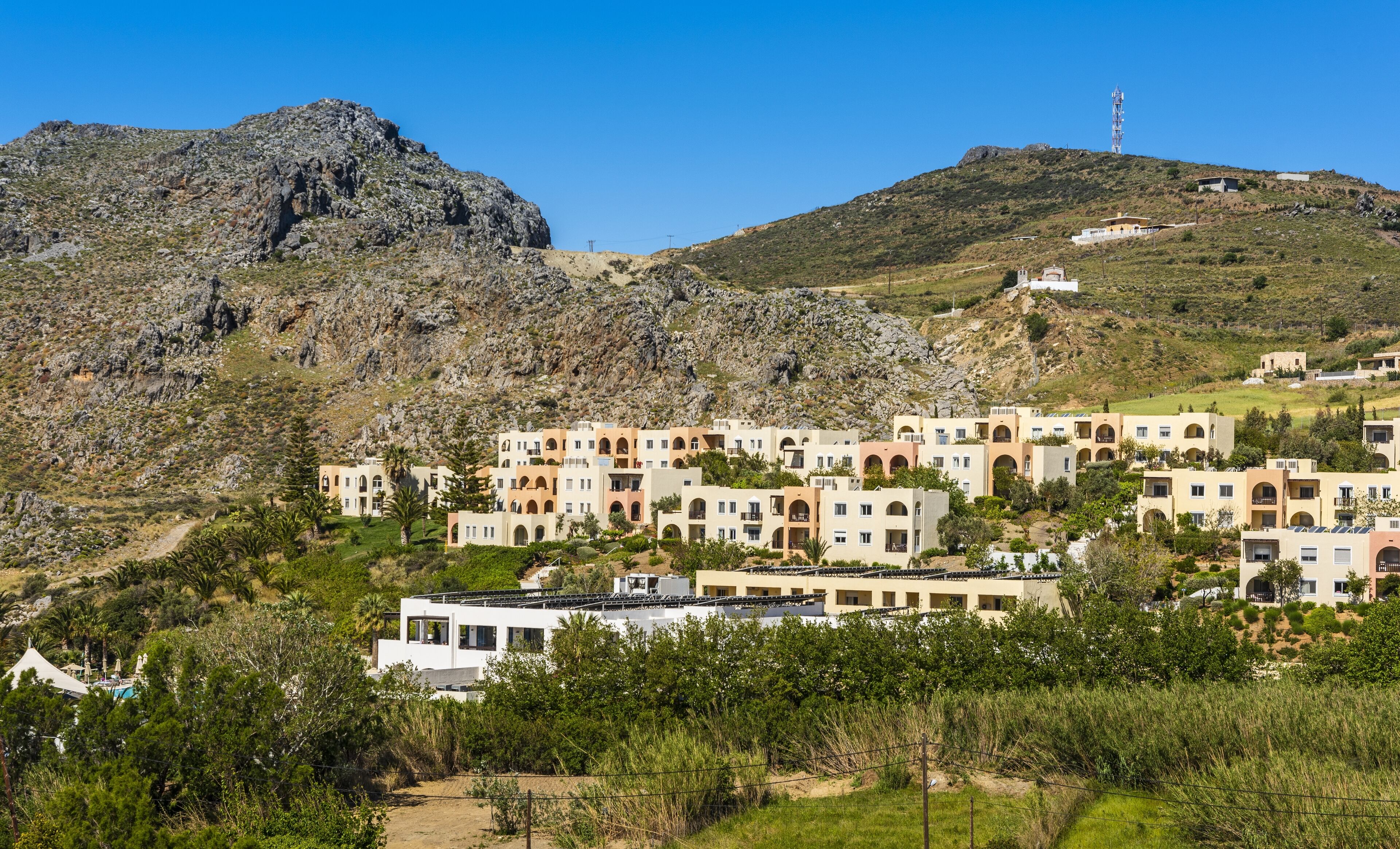 A hillside village with traditional architecture, including buildings with arches and a prominent mountain in the background.