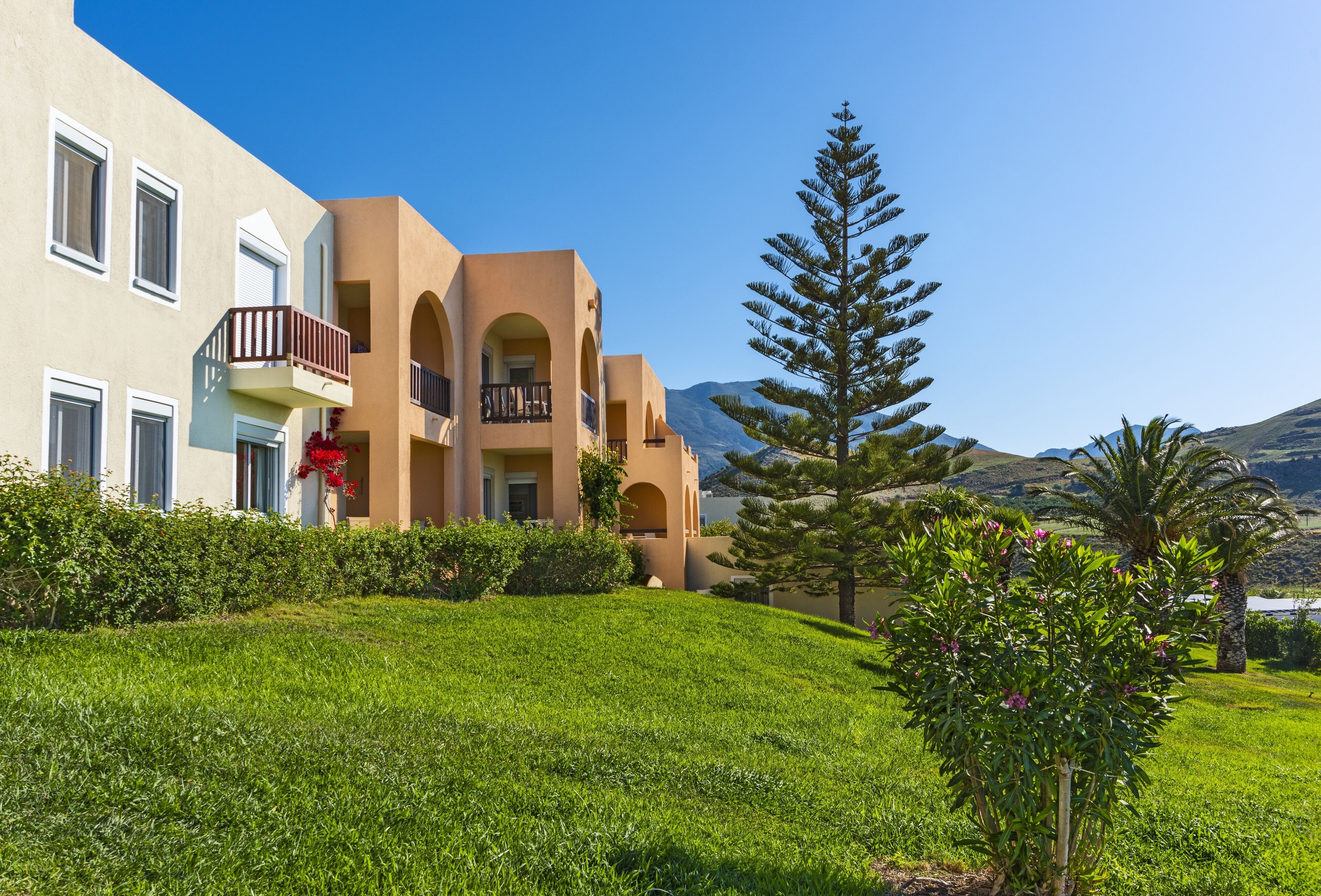 A hotel with multiple balconies, a well-maintained lawn, and a mountainous backdrop.