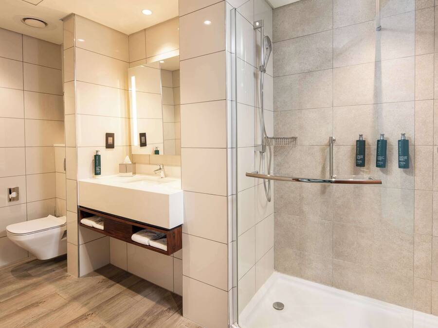 Een moderne badkamer met een douchecabine van glas, een witte wastafel en een toilet.