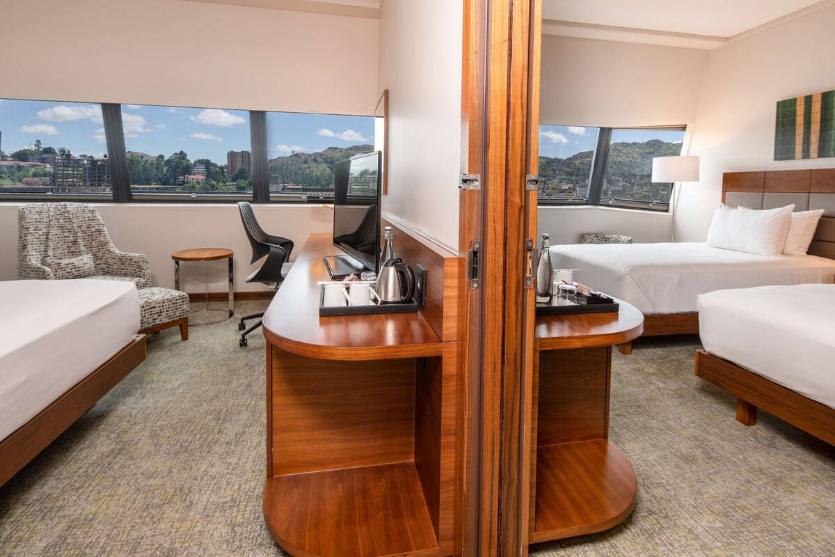 Quarto de hotel com duas camas, uma escrivaninha, uma cadeira e vista para a cidade.