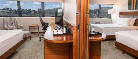 A hotel room with two beds, a desk, a chair, and a view of the city.