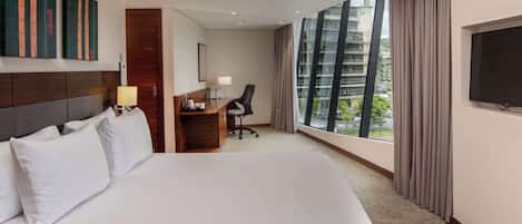 Habitación de hotel con una cama grande, un escritorio con silla, un televisor y una ventana con cortinas.
