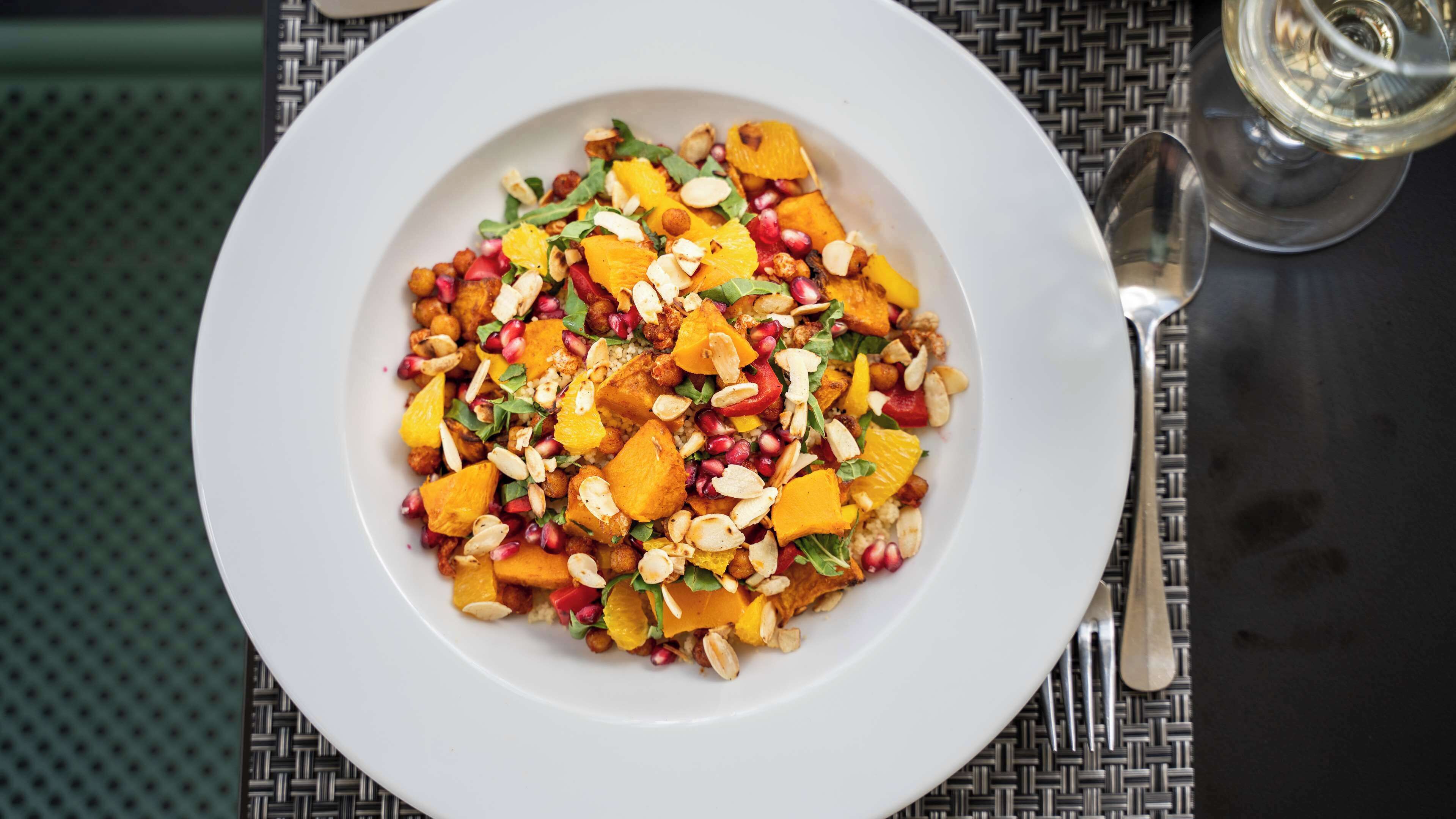 A white plate with a colorful salad on a table with a woven placemat.