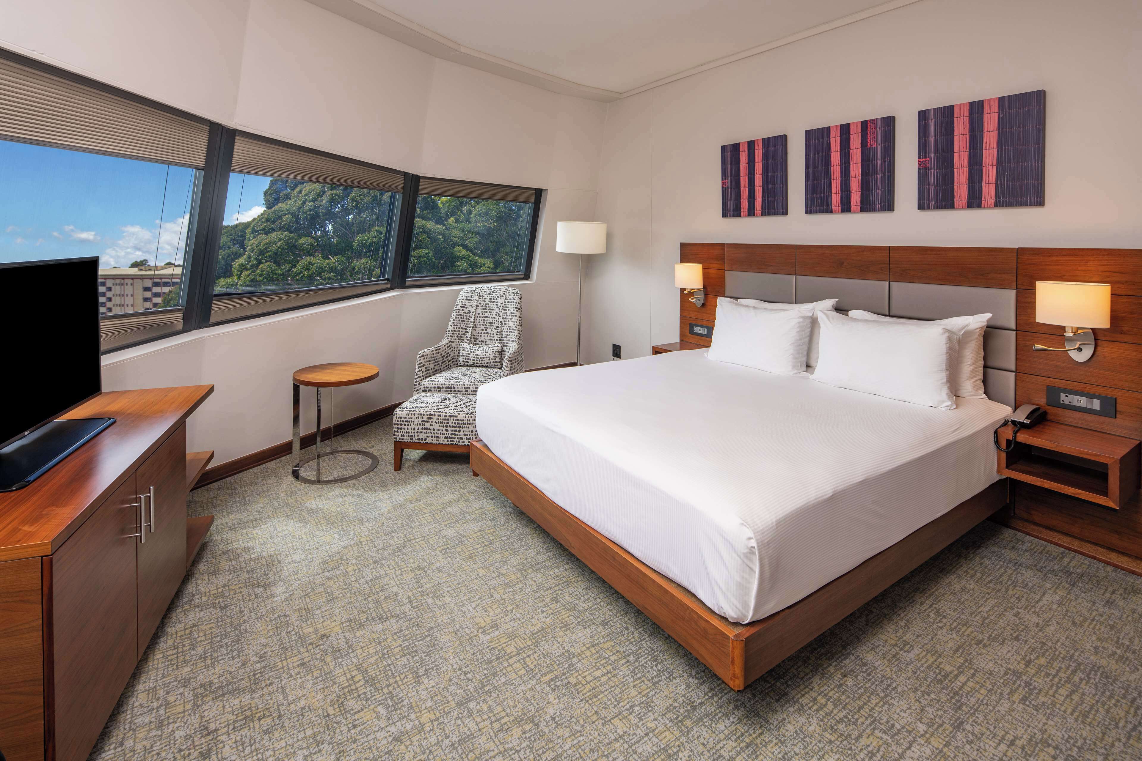 A hotel room with a large bed, a TV, a chair, and artwork on the wall.