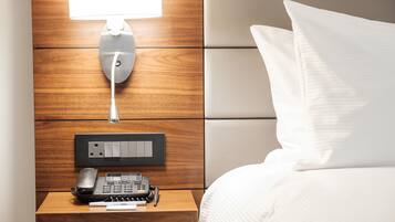 Habitación de hotel impecable con cabecera de madera, mesita de noche con lámpara, teléfono y control remoto.