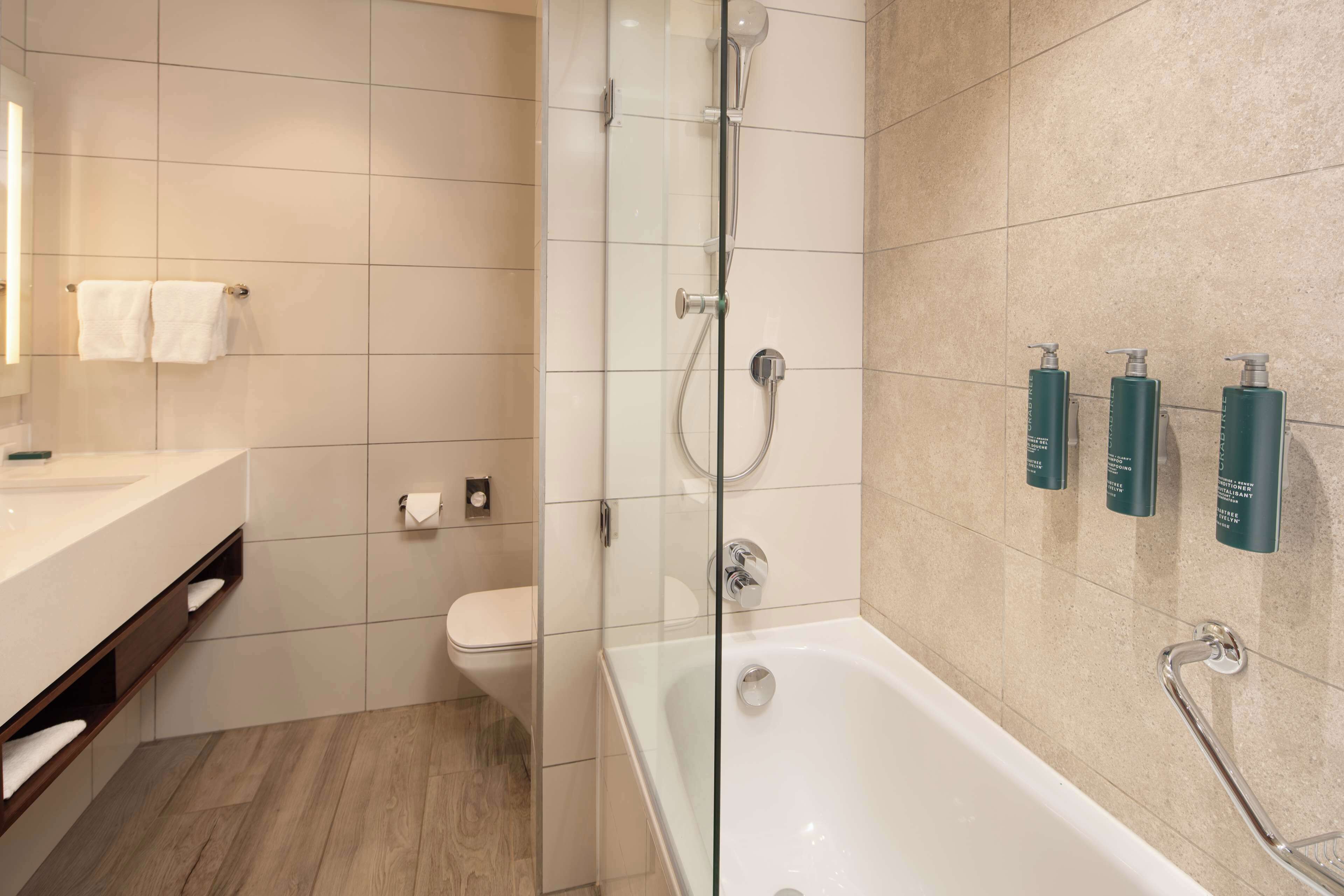 Un baño moderno con ducha envuelta en vidrio, una bañera blanca y un tocador con espejo.
