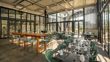 A spacious outdoor dining area with green chairs and tables, large windows, and a high ceiling.