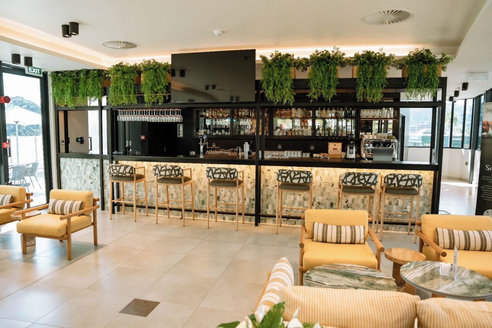 Zona de bar con mostrador, taburetes y una sala de estar con sillas y mesas.
