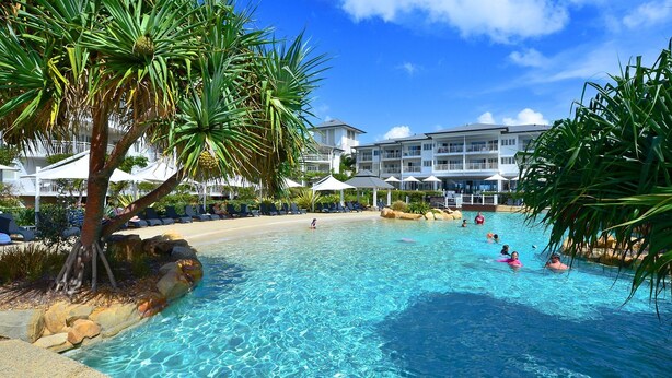 A pool area with clear blue water, lounge chairs, and a building with balconies in the background. - Resort on the Beach 4302 with resort Pool (KINGSCLIFF)