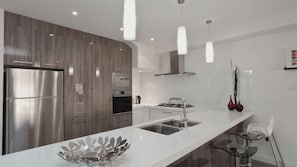 A modern kitchen with a stainless steel refrigerator, a built-in oven, a gas stove, and a white countertop.