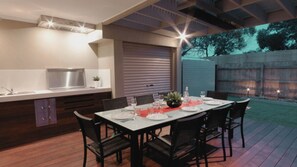 An outdoor dining area with a table set for six, surrounded by chairs, a built-in kitchen with a sink and stove, and a covered patio. - Amaroo by the beach and Swan Bay (Queenscliffe)