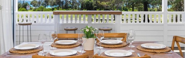 An outdoor dining area with a white fence, wooden chairs, and a table set for four. - OCEANFRONT BEACH HOUSE ON MARINE PARADE (KINGSCLIFF)