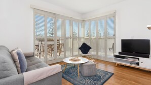 A modern living room with a grey sofa, a small round table, a white armchair, and a TV on a white stand. - Resort on the Beach 2214 15 with resort Pool (KINGSCLIFF)