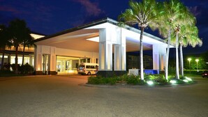 A well-lit hotel entrance with a covered waiting area, palm trees, and a taxi parked outside. - Resort on the Beach 2214 15 with resort Pool (KINGSCLIFF)