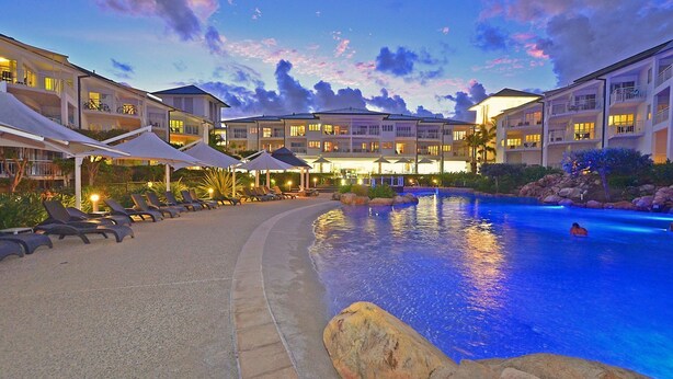 A resort pool area with lounge chairs and umbrellas, surrounded by multi-story buildings with balconies. - Resort on the Beach 2214 15 with resort Pool (KINGSCLIFF)