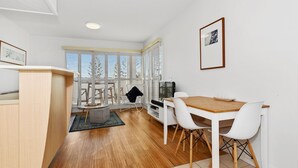A modern kitchen with a dining area, wooden flooring, and a view through large windows. - Resort on the Beach 2214 15 with resort Pool (KINGSCLIFF)