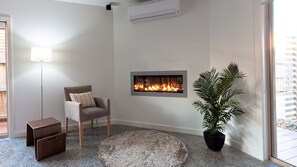 A modern living room with a fireplace, a chair, a floor lamp, a small table, and a potted plant.