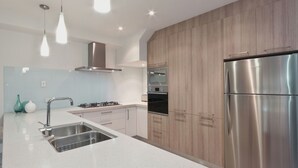 A modern kitchen with stainless steel appliances, a double sink, and wooden cabinetry. - Taworri at Swan Bay in Queenscliff (Queenscliff)