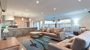 A modern living room with a sofa, coffee table, and kitchen area with bar stools. - Taworri at Swan Bay in Queenscliff (Queenscliff)