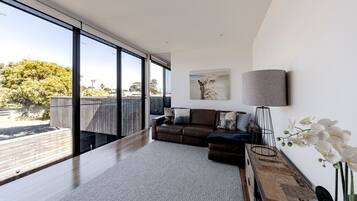 A modern living room with a large window, a brown leather sofa, a grey rug, and a minimalist lamp.