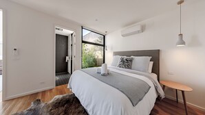 A modern bedroom with a large bed, a small bedside table, and a view of the outdoors. - Stella on Stevens in Queenscliff (Queenscliff)
