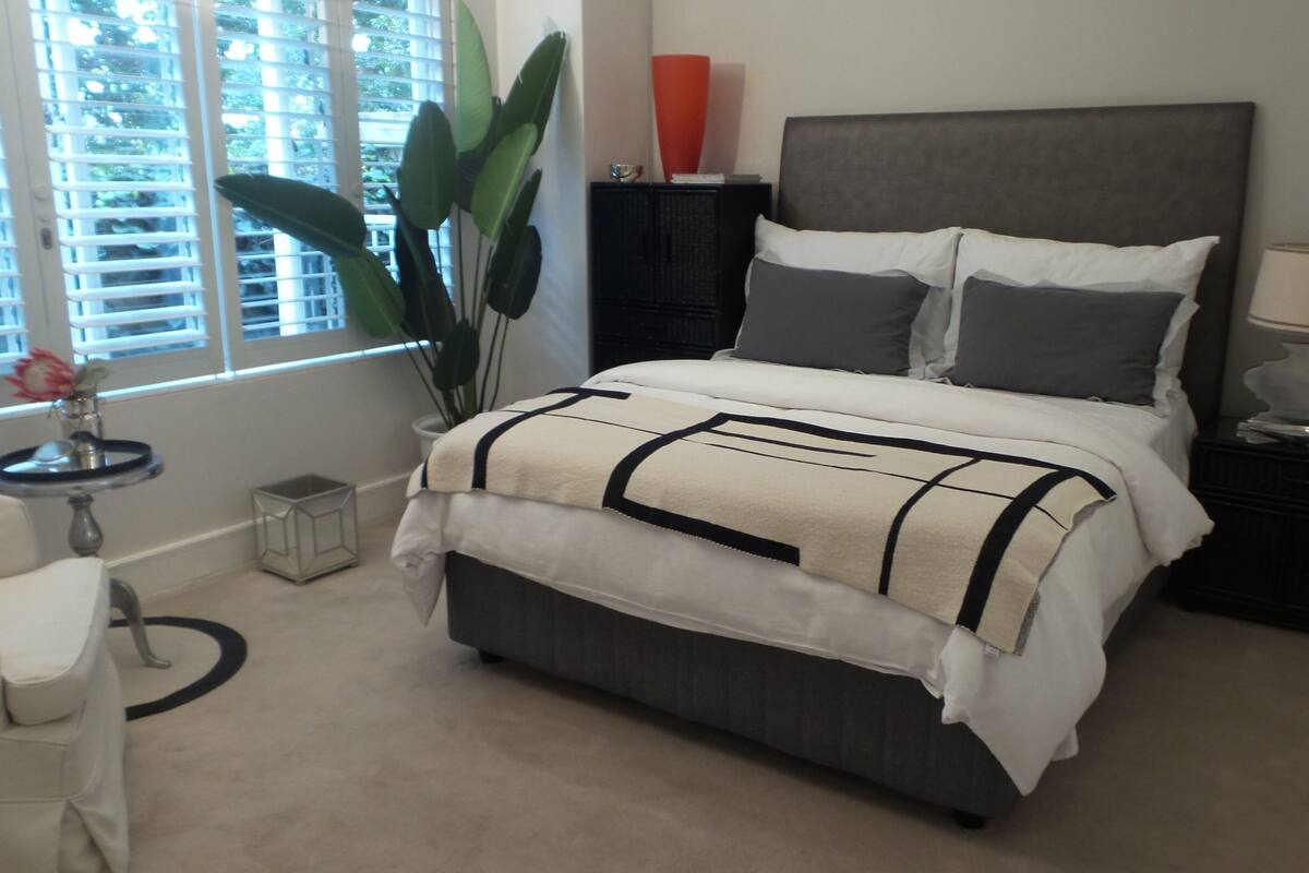 Ein Schlafzimmer mit Bett, Nachttischen, einer Lampe, einem Blumentopf und einem Fenster mit Jalousien.