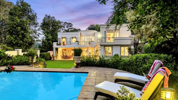 Une maison moderne dotée d’une piscine, de chaises longues et d’un jardin bien entretenu.