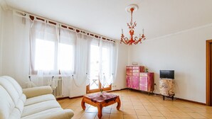 Un saló amb un sofà, una taula de centre de fusta, un llumíger, una televisió sobre un moble i una finestra amb cortines.