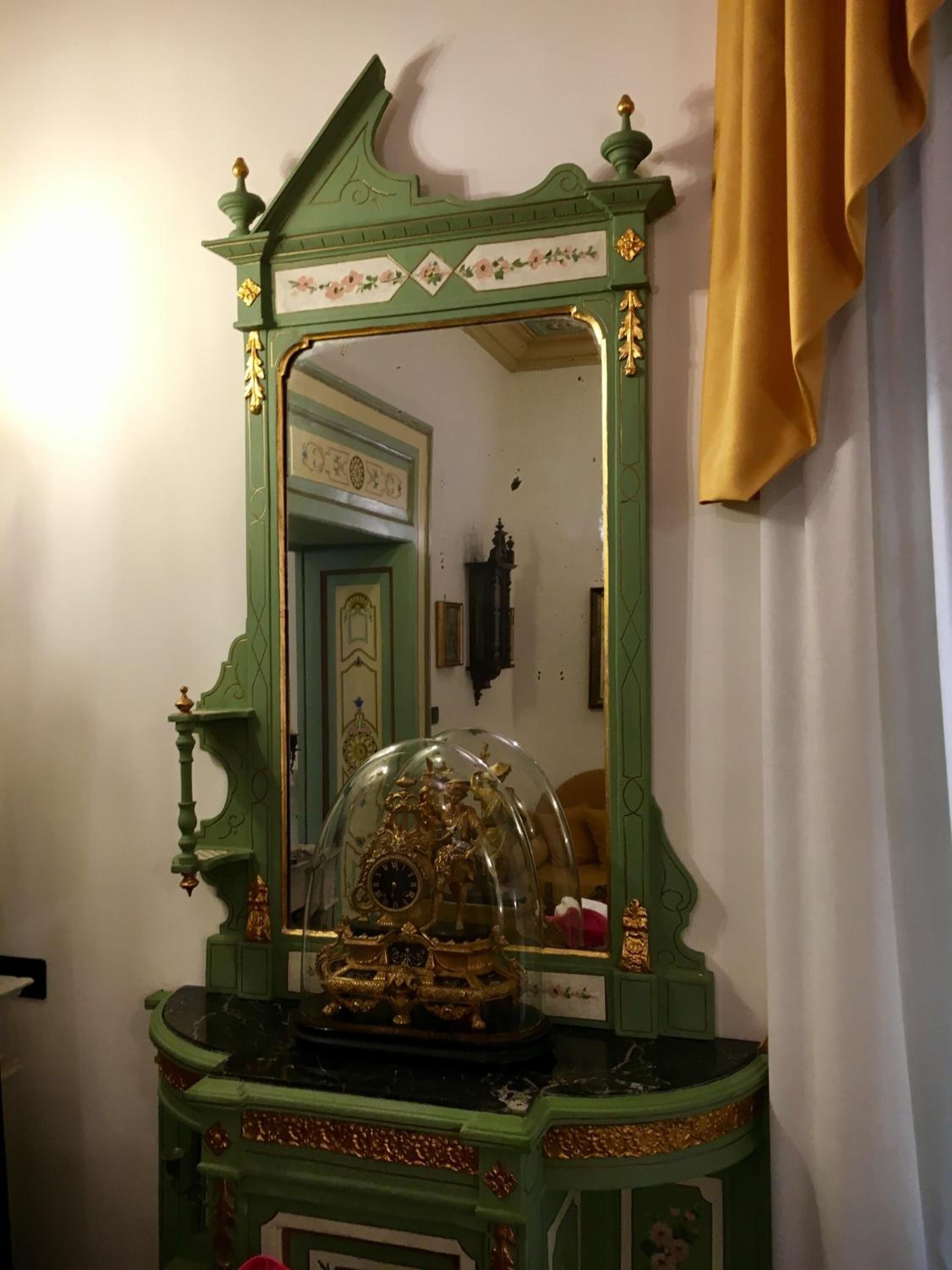 A green ornate mirror with a clock and decorative elements.