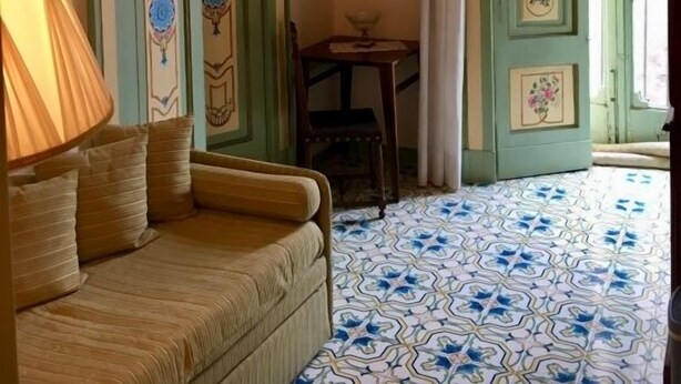 Une pièce dotée d’un sol à motifs, d’un canapé, d’un lustre et de portes vertes ornées de panneaux décoratifs.