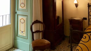 Une pièce avec une porte verte, une chaise en bois, un meuble en bois et un lit recouvert d’une couvre-lit à motifs.