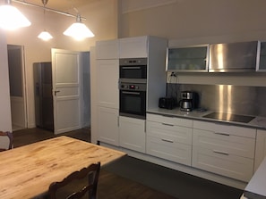 Una cocina moderna con armarios blancos, horno empotrado, cafetera y campana extractora de acero inoxidable.