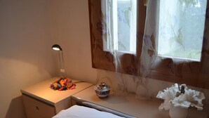 Una camera da letto con un letto, un comodino con una lampada, una finestra con tende floreali e un vaso con fiori.