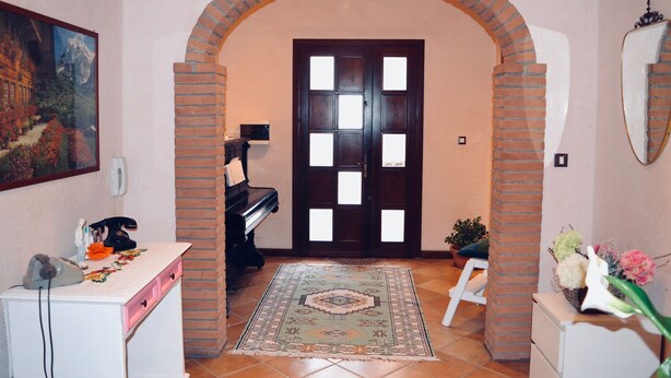 Un corridoio con un pianoforte, una scrivania con il telefono, un tappeto e una porta con arco in mattoni.