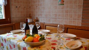 Un tavolo da pranzo apparecchiato con una tovaglia floreale, una ciotola di frutta, bicchieri da vino e una bottiglia di vino.