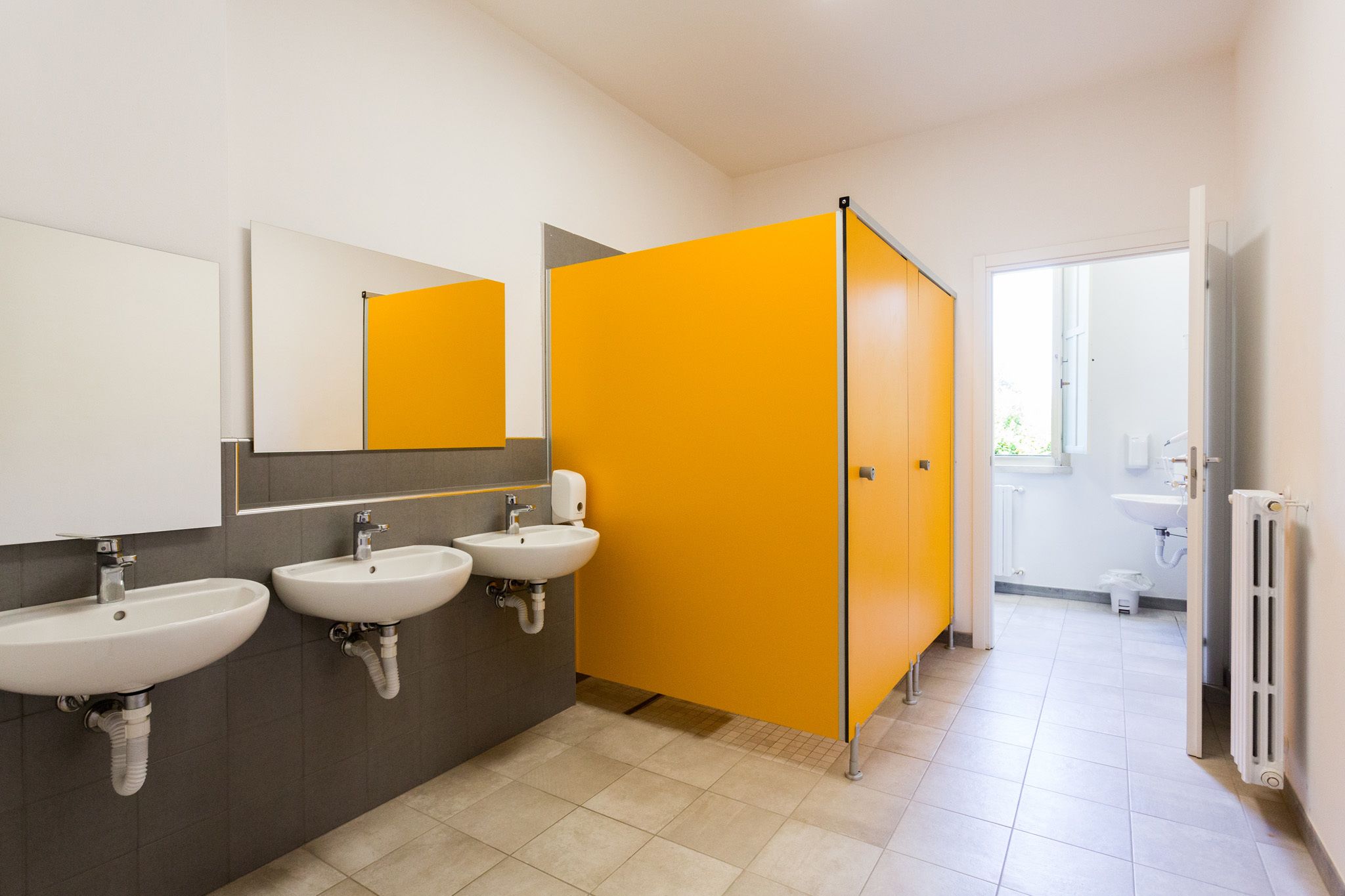 Un baño moderno con tres lavamanos, un espejo y una mampara amarilla.