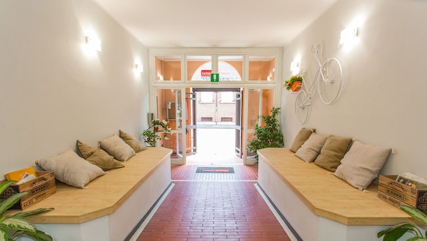 Una zona de recepción con piso de ladrillo, dos áreas de descanso con cojines, plantas en macetas y una decoración de bicicleta en la pared.