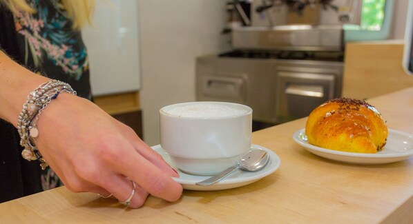 A person serving a white cup of coffee and a pastry on a wooden table.