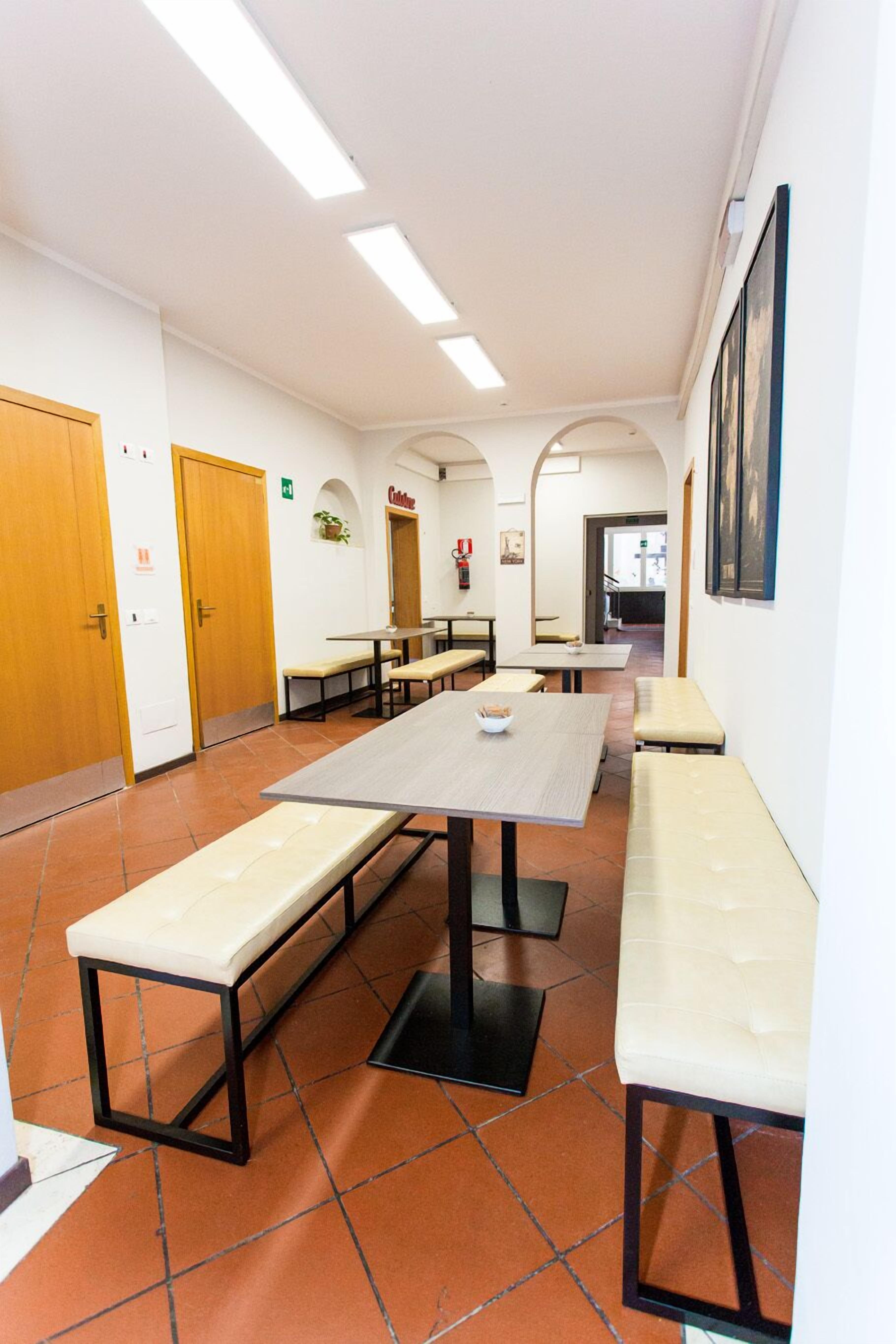 Un comedor con mesas y bancos largos, un extintor y una puerta que indica "Cafetería".
