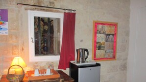 Une petite cuisine équipée d’une table, de chaises, d’un réfrigérateur, d’une bouilloire, d’une fenêtre avec un rideau et d’un mur orné d’un tableau encadré.