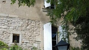 Un bâtiment en pierre avec des volets blancs, une porte en verre et une table avec des chaises à l’extérieur.