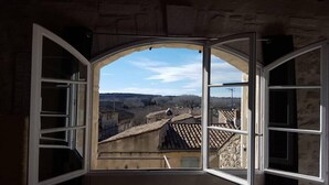 Une pièce dotée d’une fenêtre en arc donnant sur une vallée où se trouvent des bâtiments construits en terrasses.