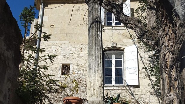 Une fontaine en pierre à plusieurs niveaux, entourée de plantes en pot et d’arbres.