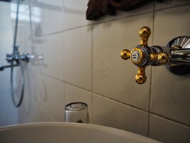Un baño con grifo dorado, un recipiente de vidrio y un cabezal de ducha.