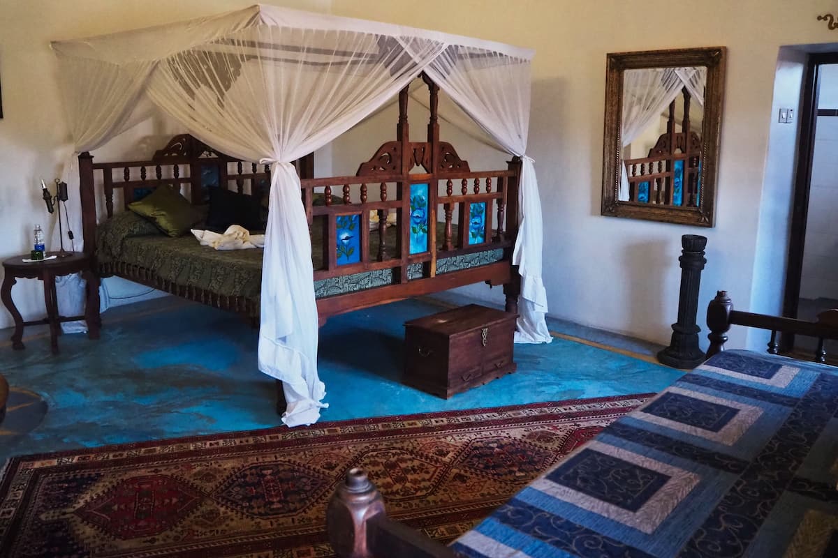 A traditional bed with a canopy, a wooden nightstand, a bedside table, a mirror, and a patterned rug.