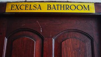 Une porte en bois avec une pancarte jaune au-dessus, sur laquelle on peut lire : « SALLE DE BAINS EXCELSA ».