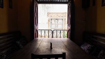 Una habitación con una mesa de madera y bancos, un balcón con barrotes y vistas a un espacio exterior con un muro de piedra.