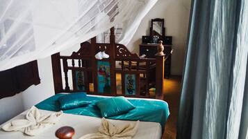 Ein Bett mit Baldachin, Türkis-farbenen Kissen und einem Holzkopfende mit Blumenmuster.