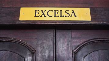 Una puerta de madera con una placa de latón que dice 'EXCELSA'.